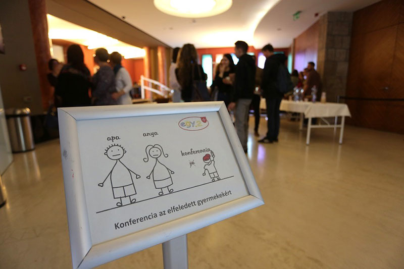 a háttérben beszélgető emberek, az előtárben a konferencia logója egy táblán