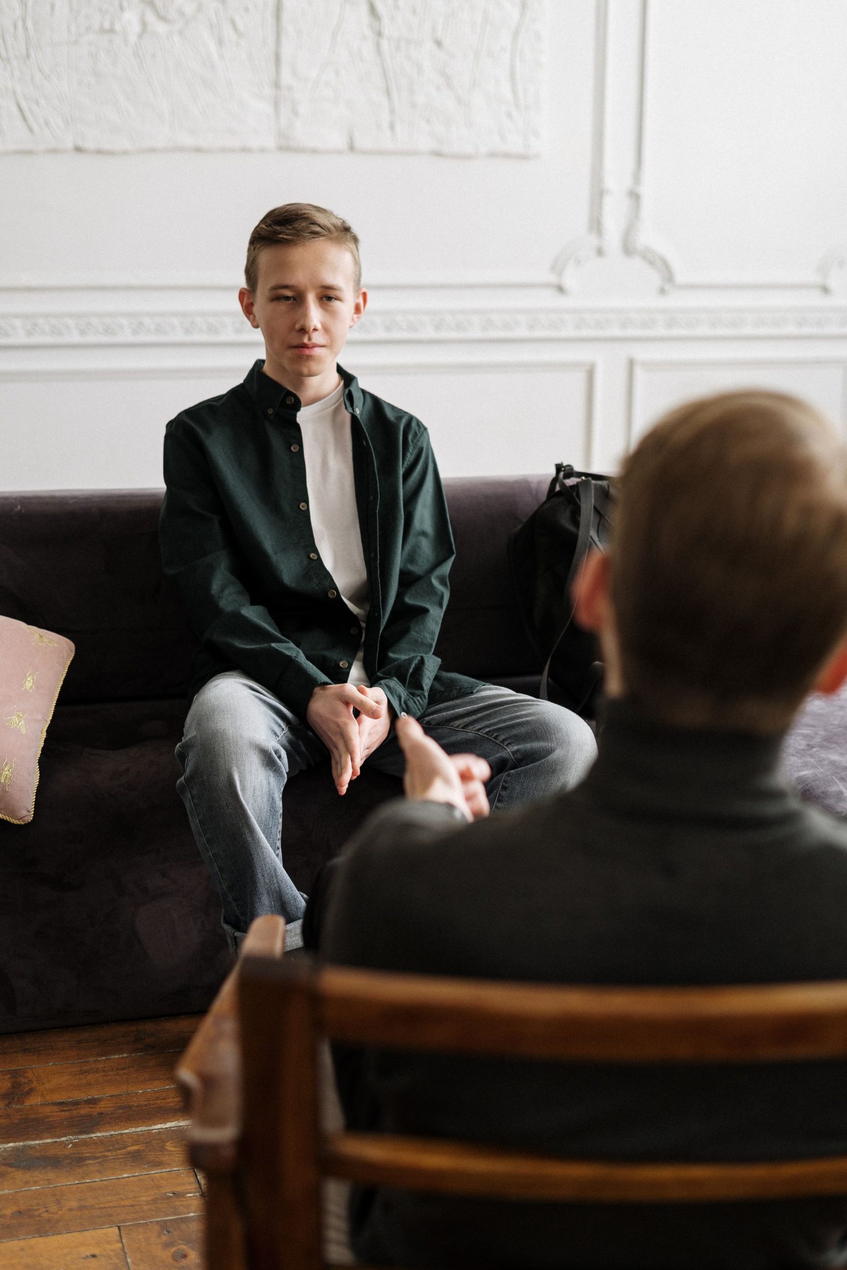két férfi ül egymással szemben, a kliens, egy fiatal férfi velünk szemben ül fekete ingben, egy kanapén